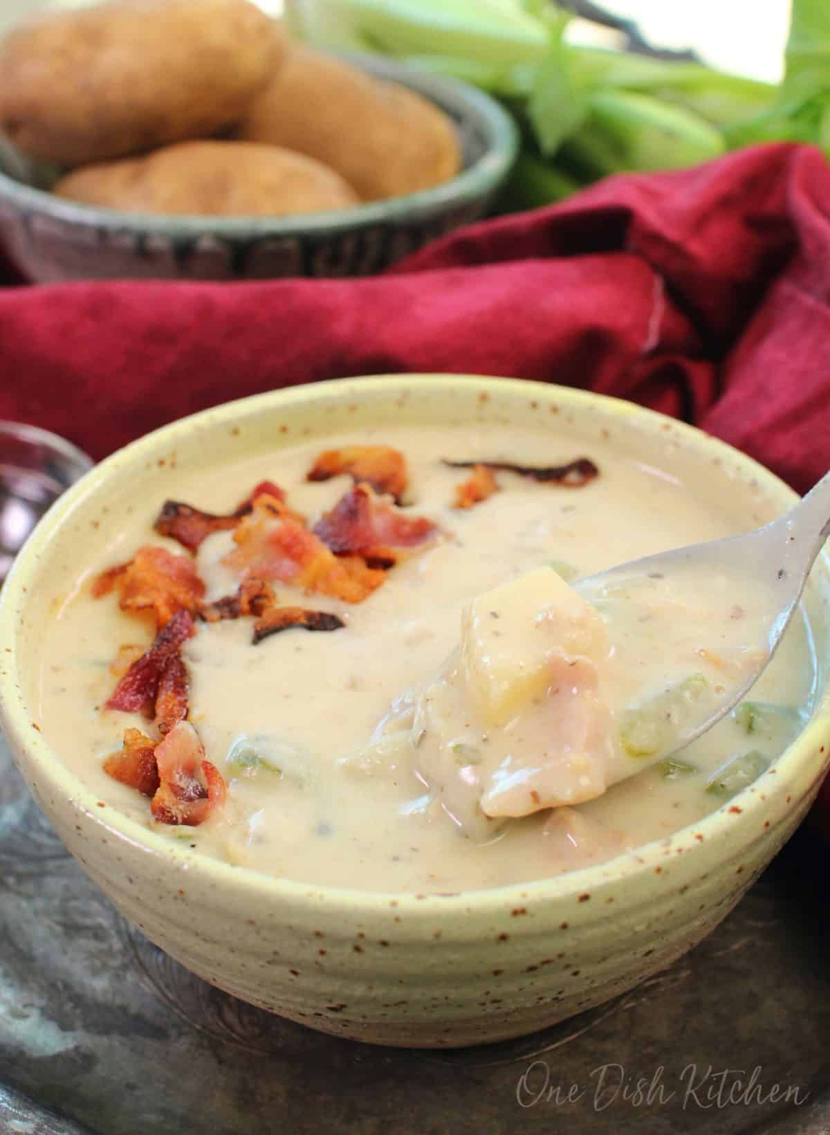 a yellow bowl of clam chowder on a tray next to a red napkin.