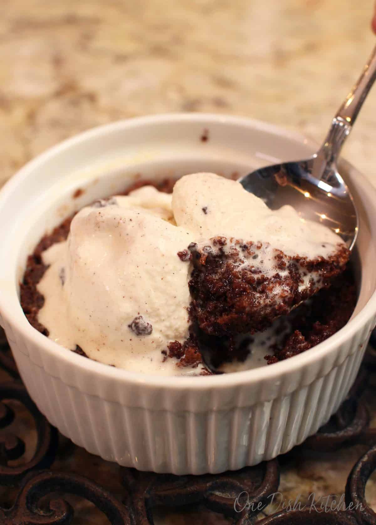 a brownie baked in a ramekin with ice cream on top and a spoon digging into the brownie.