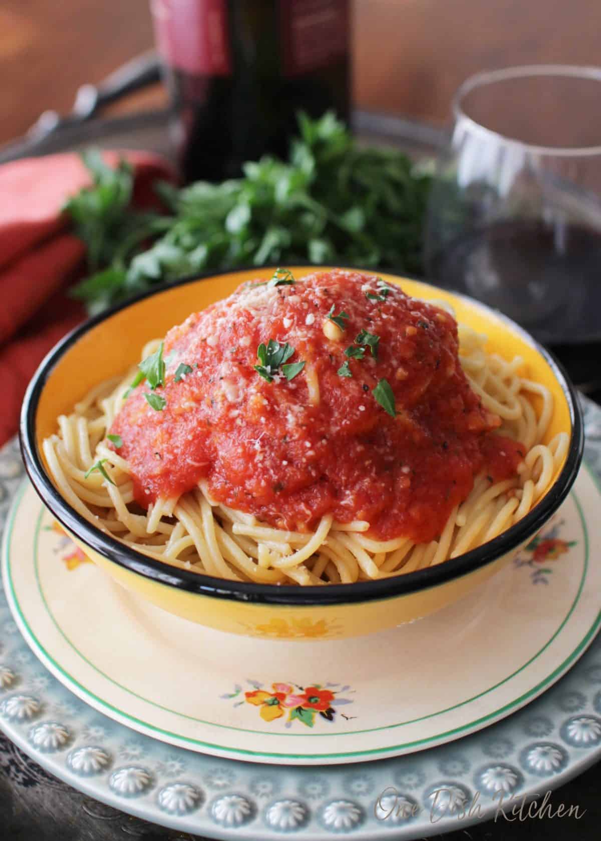 A bowl of pasta topped with tomato sauce plated on a metal tray with a glass of red wine
