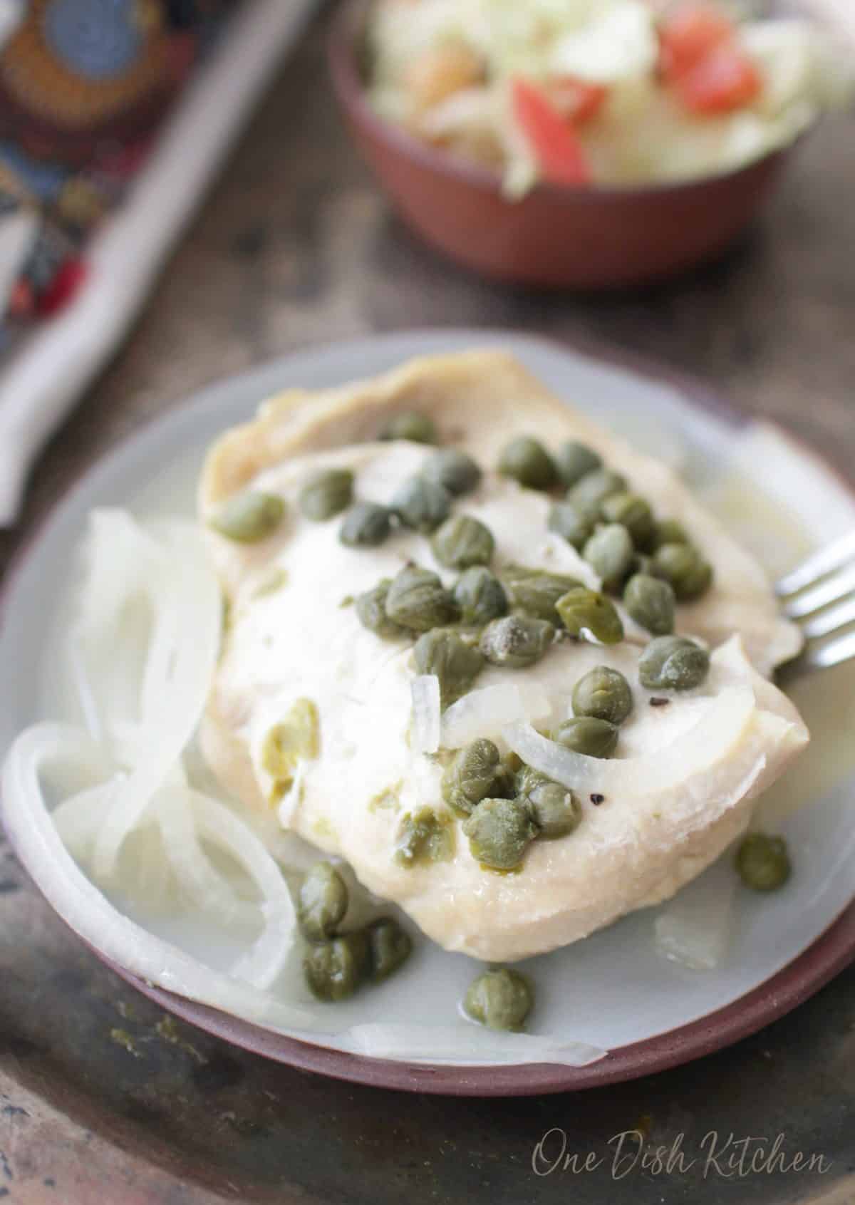 Chicken piccata on a plate topped with capers and chopped onions