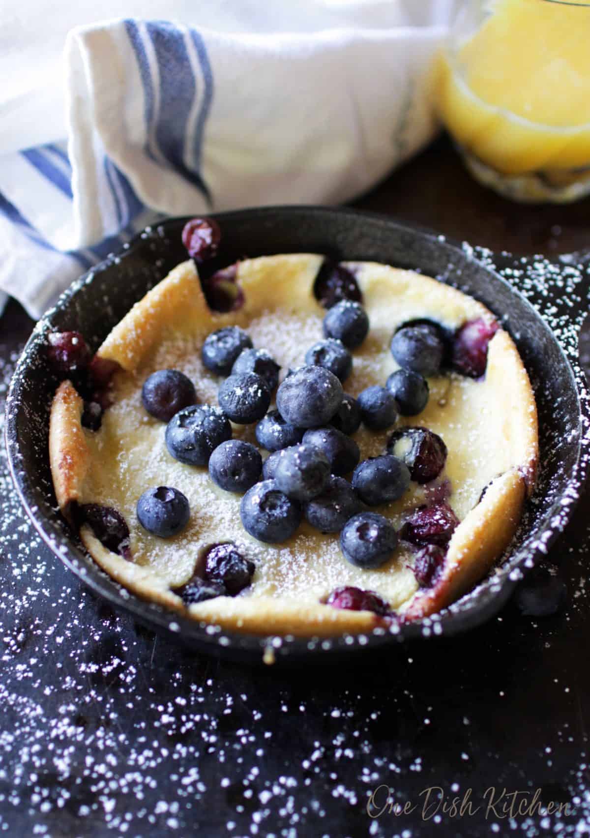 A dutch baby pancake topped with blueberries and powdered sugar in a small cast iron skillet.