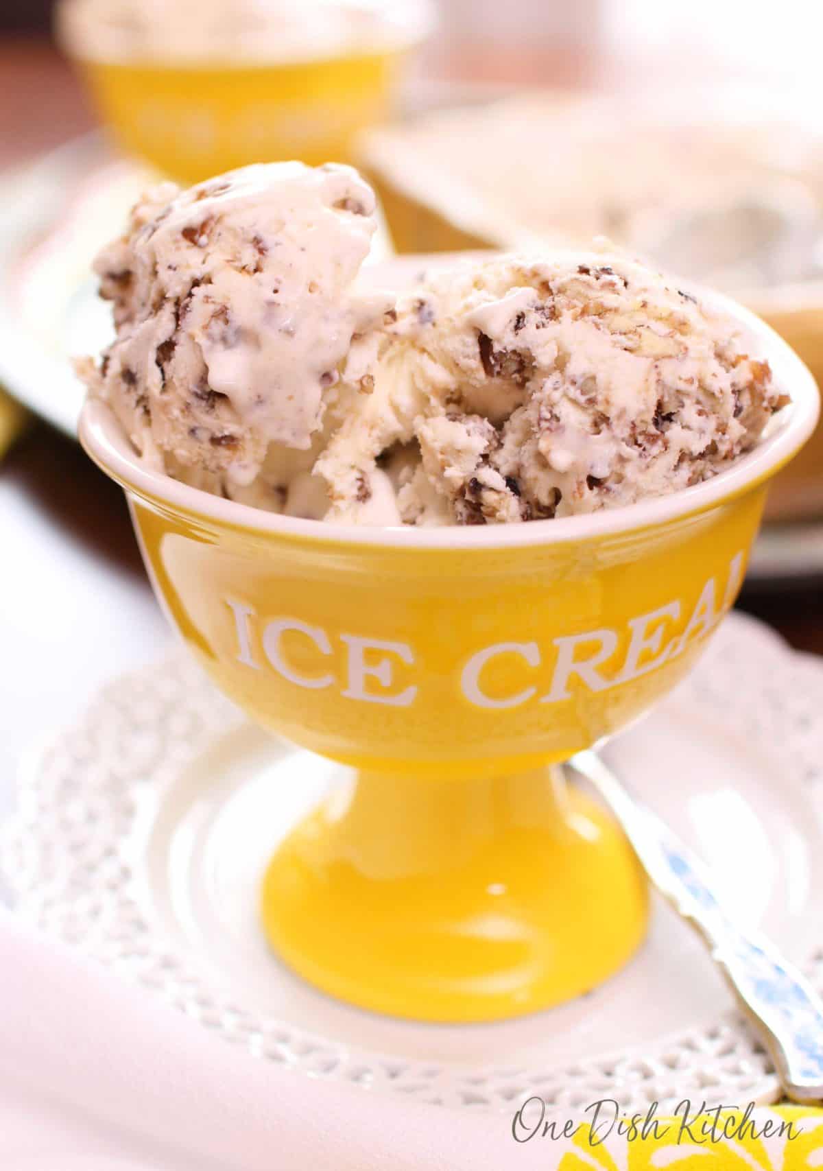 A yellow dessert bowl filled with two scoops of butter pecan ice cream.