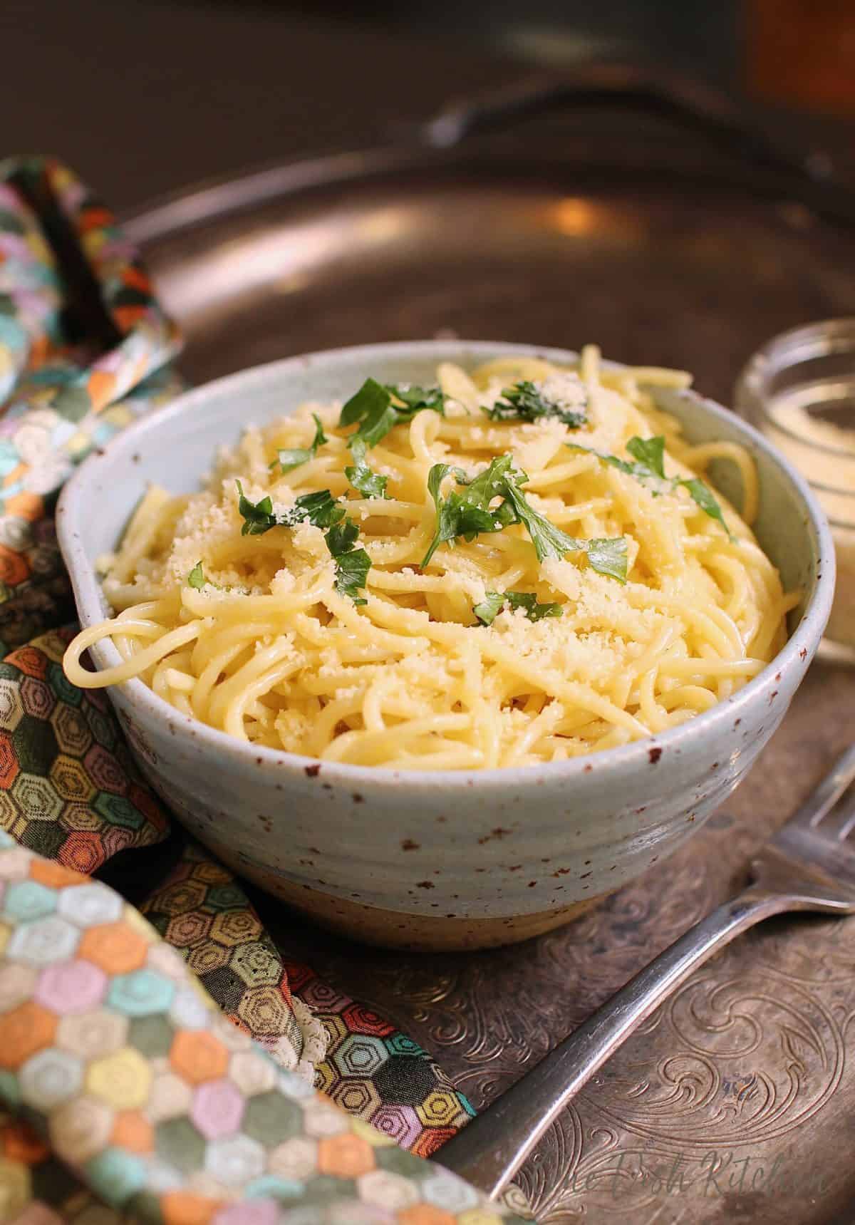 Spaghetti noodles topped with parmesan cheese and chopped parsley in a bowl next to a fork on a metal tray