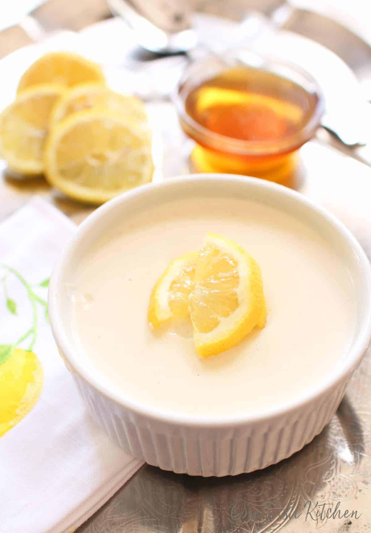 Honey lemon custard in a small ramekin next to sliced lemons and a small bowl of honey all on a metal tray