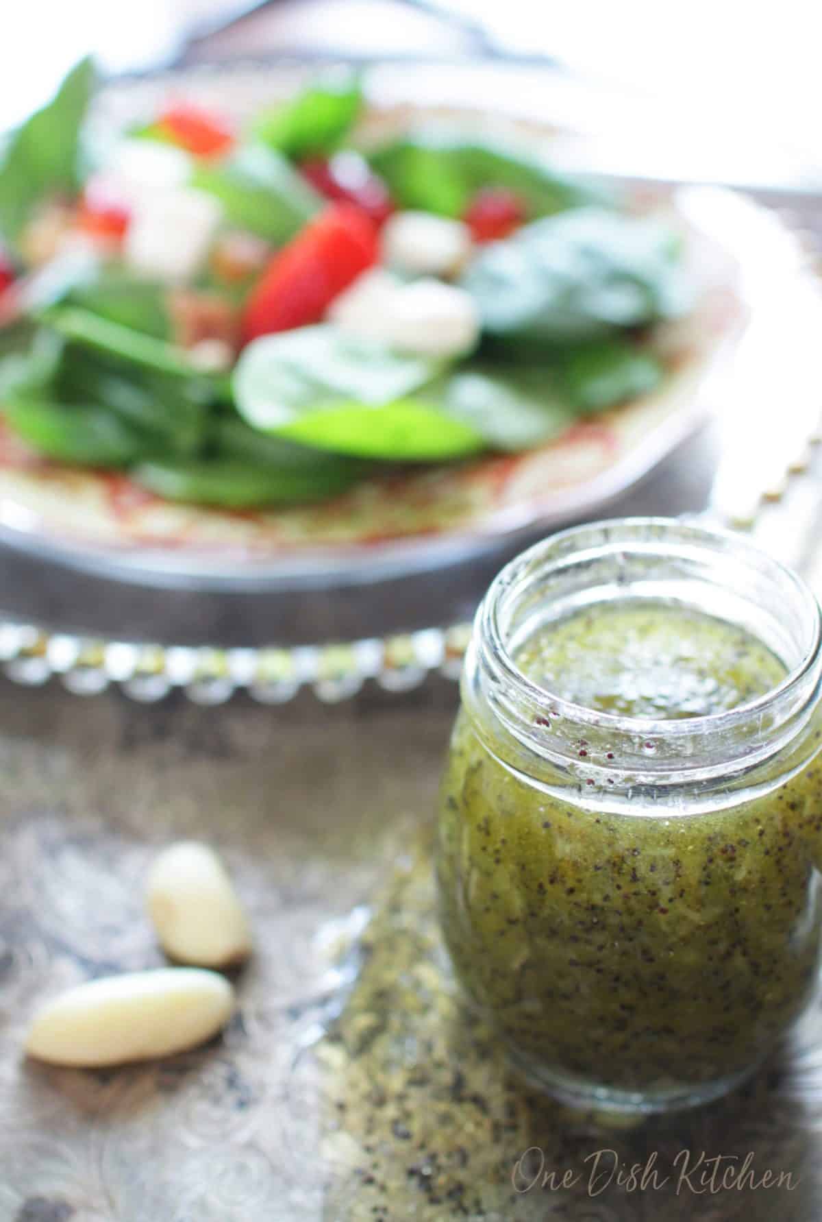 a jar of salad dressing on a silver tray next to a salad on a red plate.