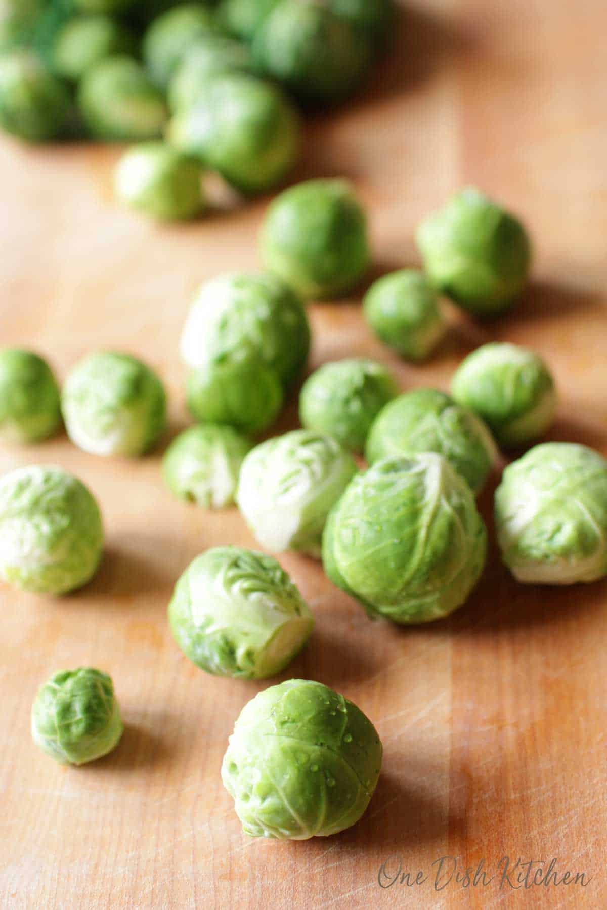 Raw brussels sprouts scattered on a wooden cutting board