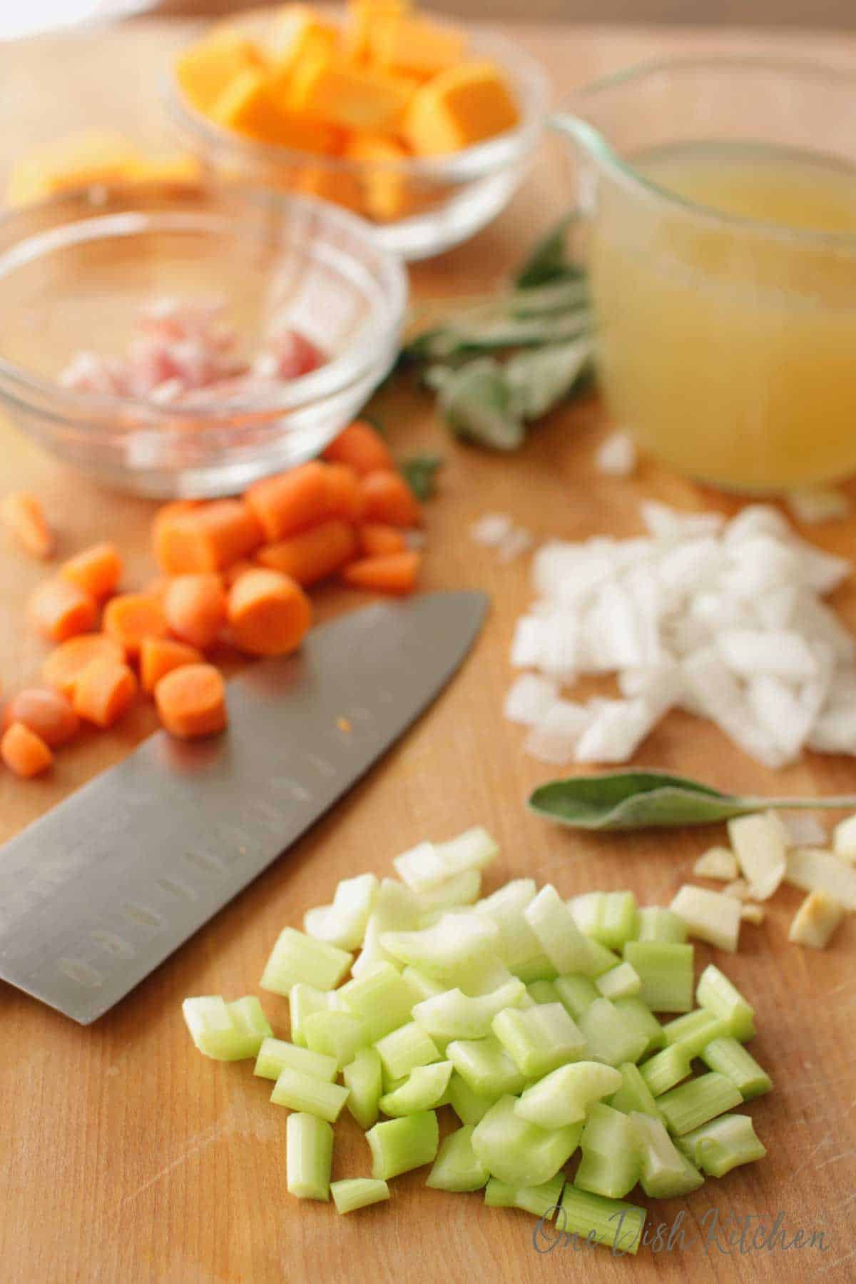 Ingredients needed in and Instant Pot Butternut Squash Soup- chopped celery, garlic, onions, carrots, butternut squash, chicken broth in a measuring cup, sage, all next to a large cutting knife