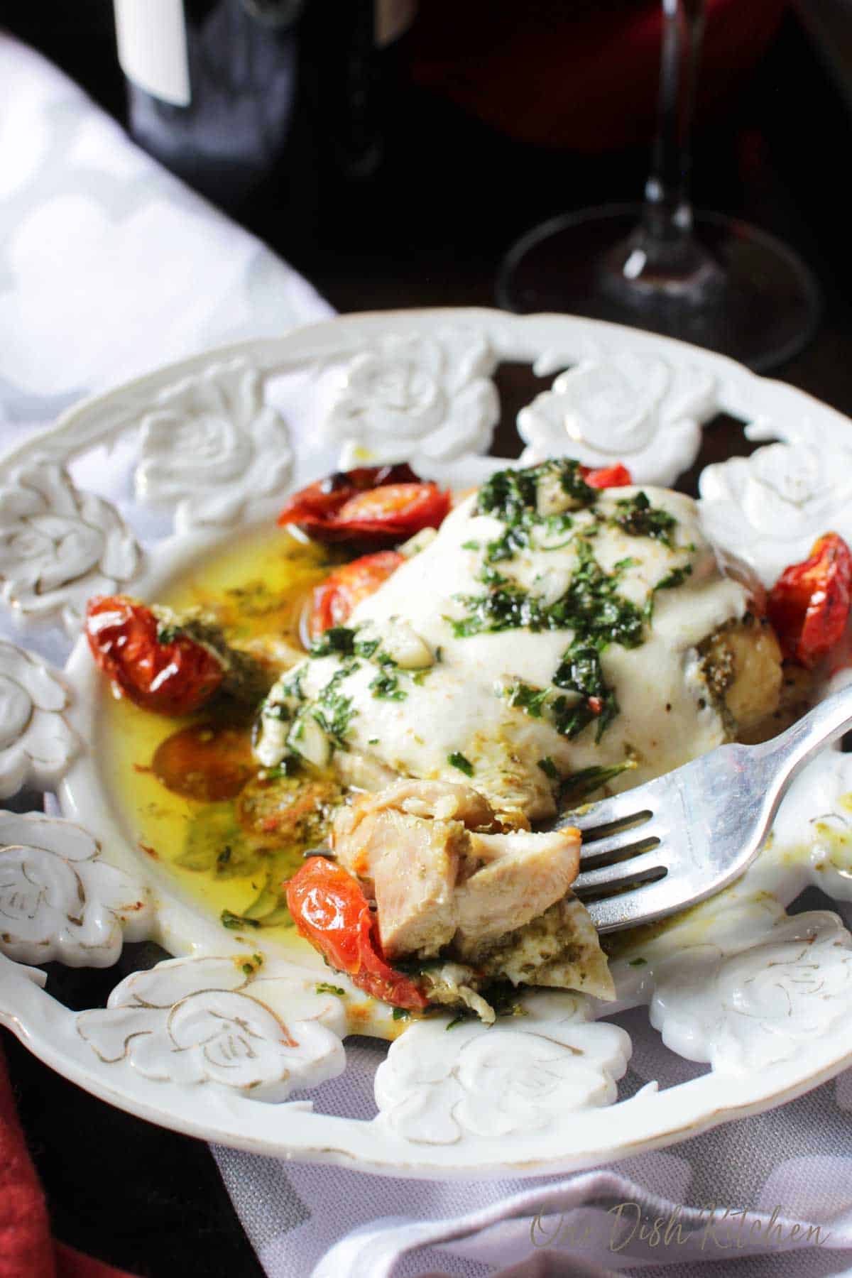 a chicken breast on a white plate topped with cheese and tomatoes