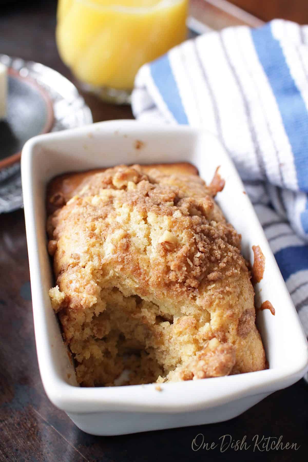 A slice of a maple walnut muffin cut out of the muffin loaf with a small glass of orange juice in the background
