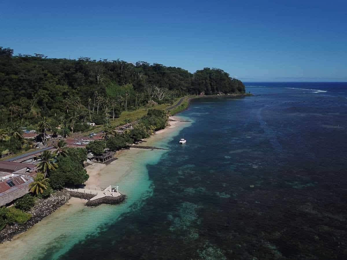 Samoa Accommodation Guide cover photo - drone shot above a hotel located next to the ocean along the coast line