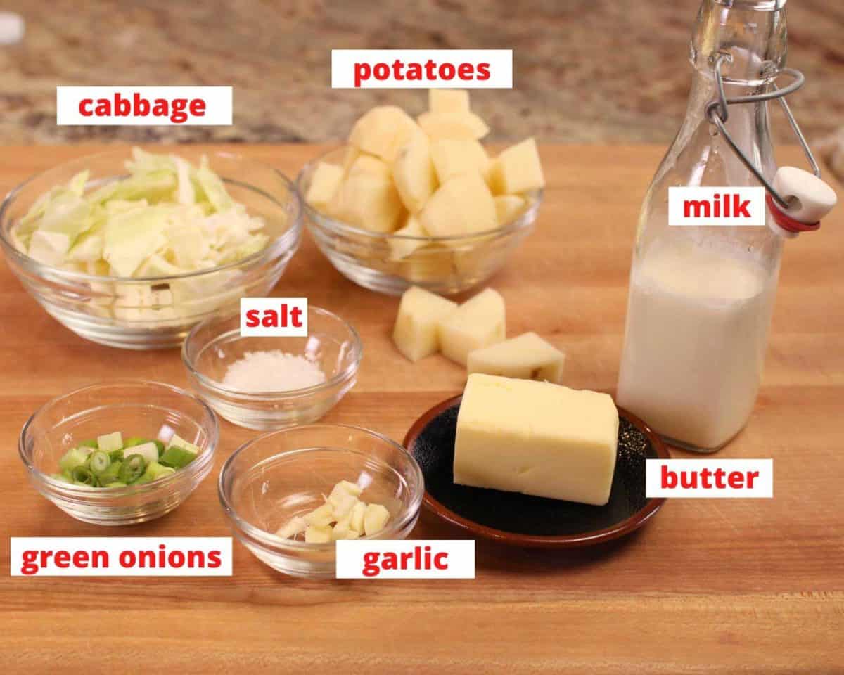 small bowls of diced potatoes, cabbage, salt, garlic, butter, and milk on a brown wooden cutting board