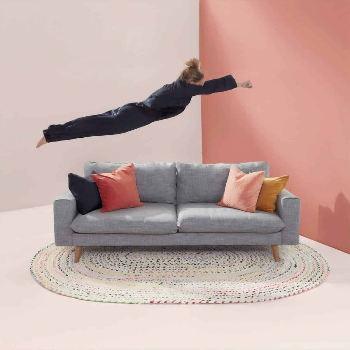 How to Travel at Home - woman 'fyinf' above a grey 2 seater couch