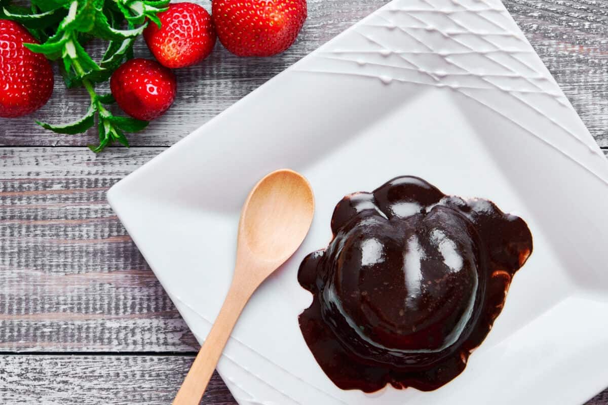 Rich decadent chocoalte mug cake served on a white plate with strawberries.
