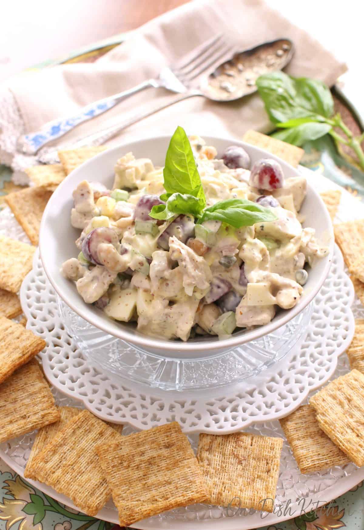white bowl filled with chicken salad surrounded by wheat crackers.