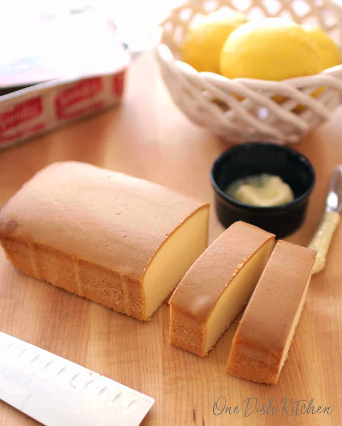 slices of pound cake on a cutting board next to a bowl of butter and a bowl of lemons.