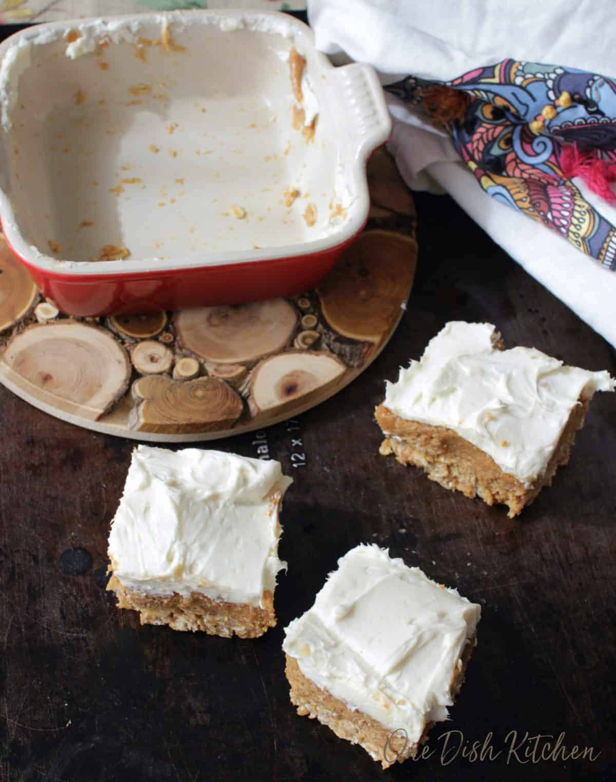three peanut butter bar squares on a black table next to an empty dish.