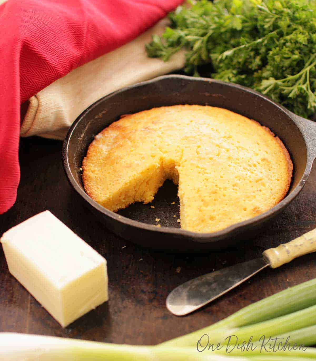 Cornbread in a small cast iron skillet next to a stick of butter and a butter knife