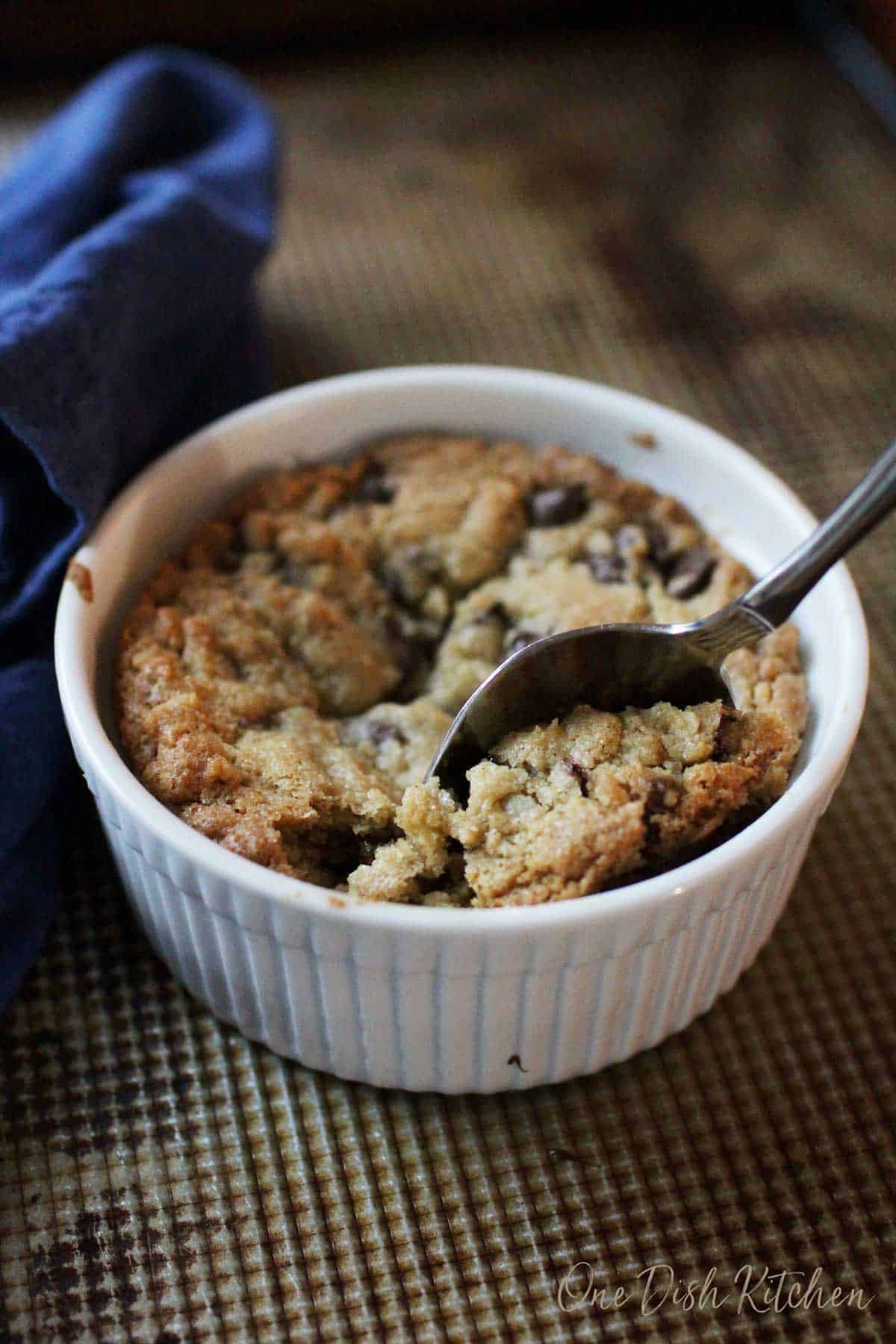 A spoonful of a deep dish cookie filled with chocolate chips from a ramekin