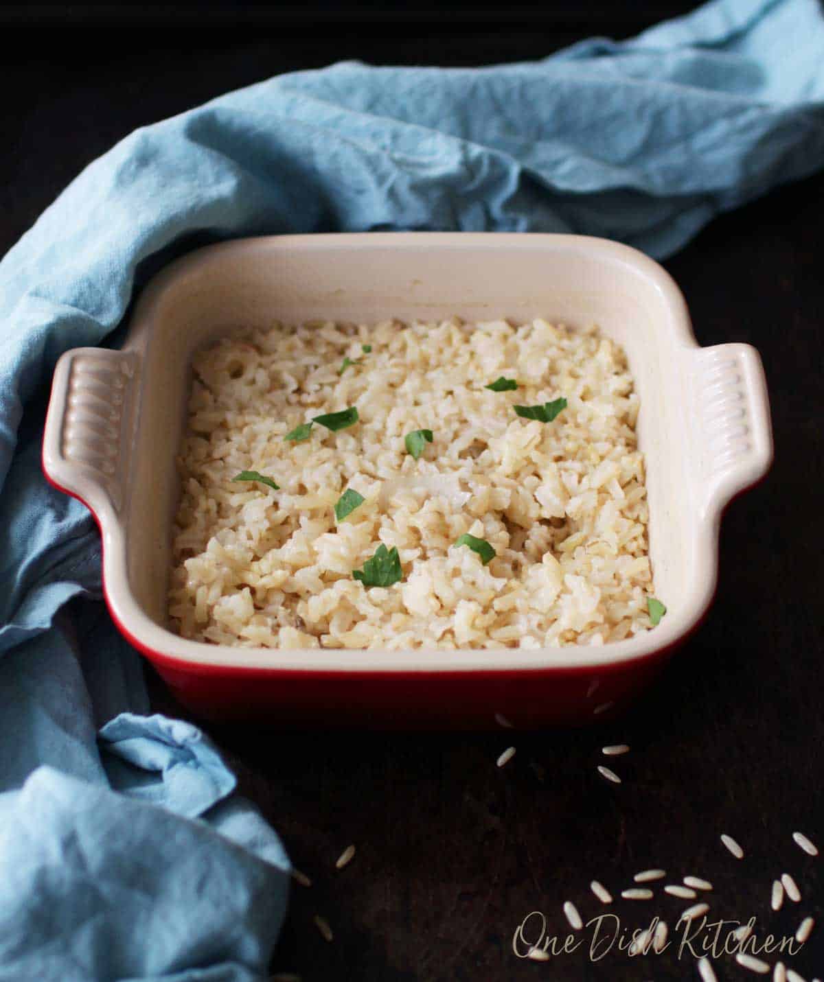 Brown rice baked in a small baking dish next to a blue cloth napkin