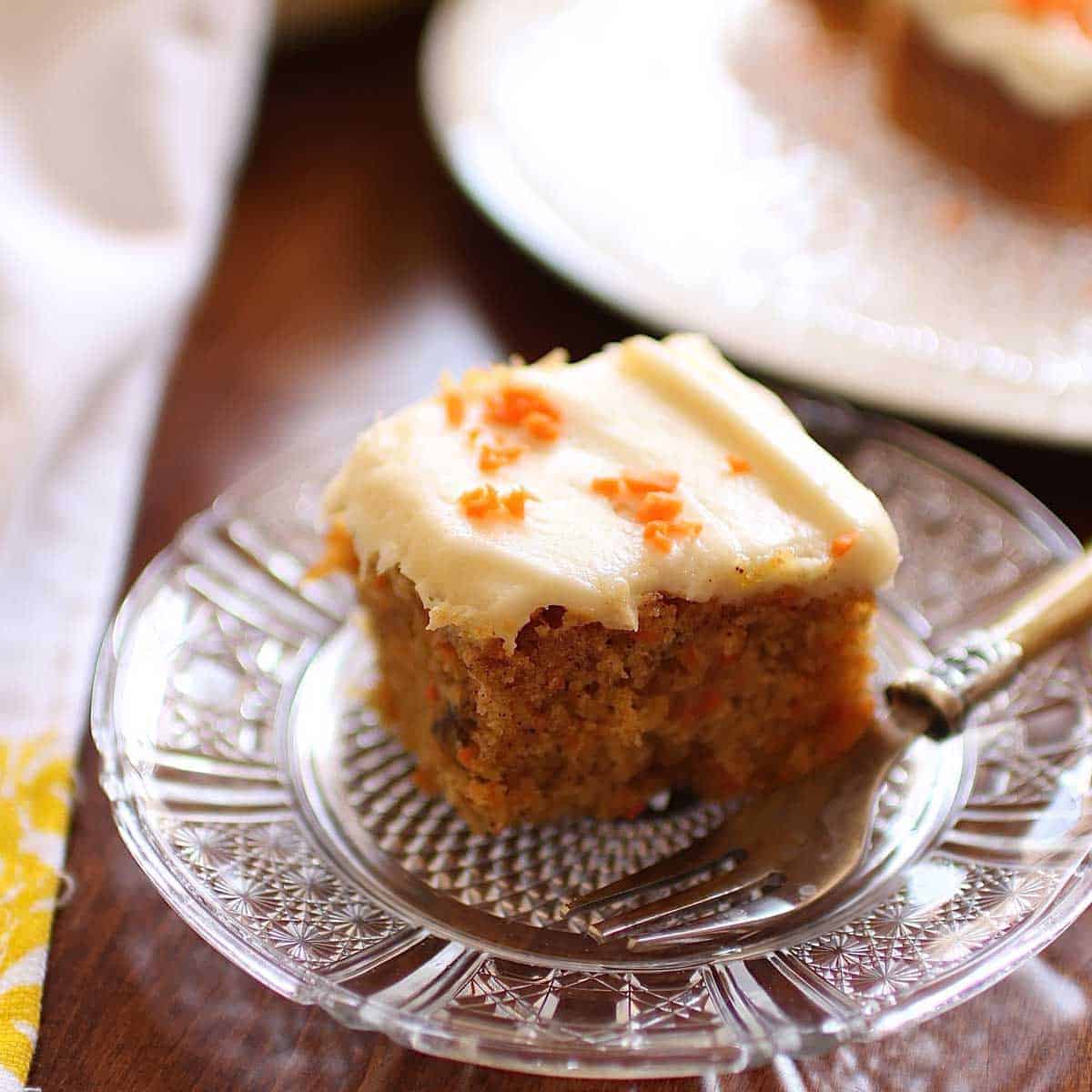 A square slice of carrot cake on a small plate with a fork