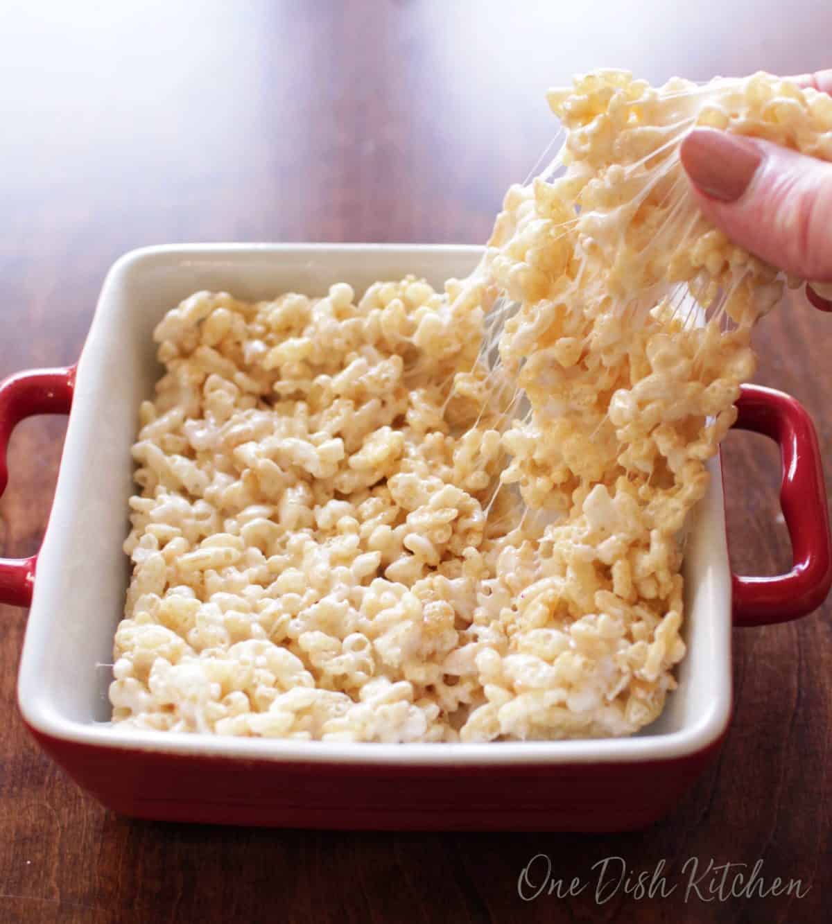 Pulling off a piece of a rice krispie treat with fingers from a small baking dish