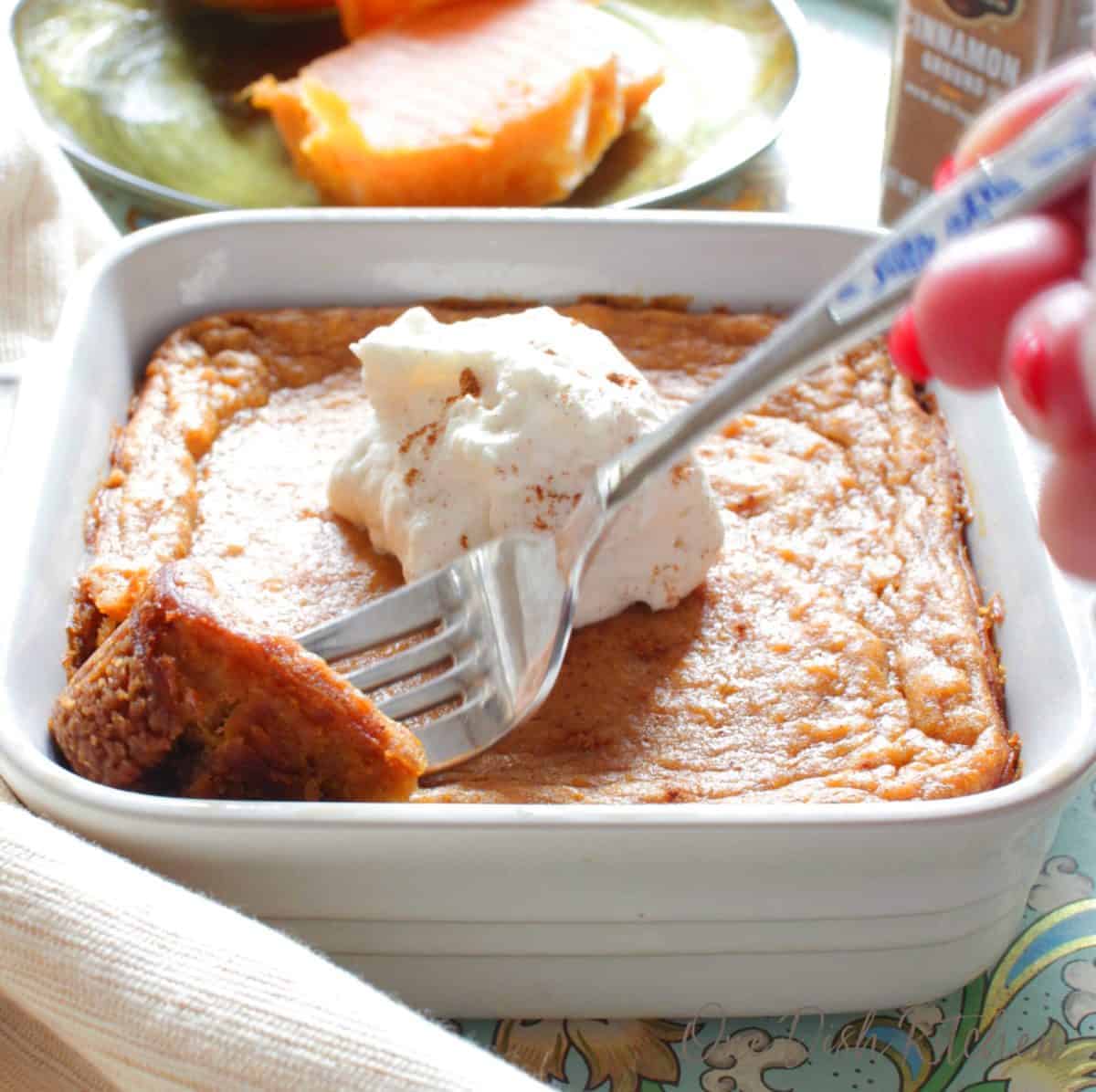 A fork grabbing a piece of sweet potato pie topped with whipped cream