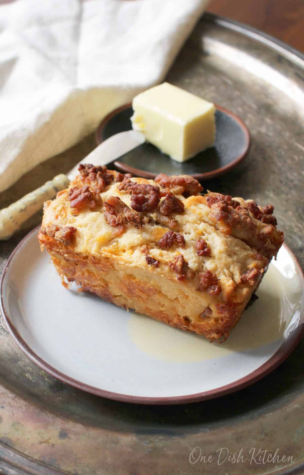 A mini loaf of sausage beer bread on a tray next to a small plate of butter