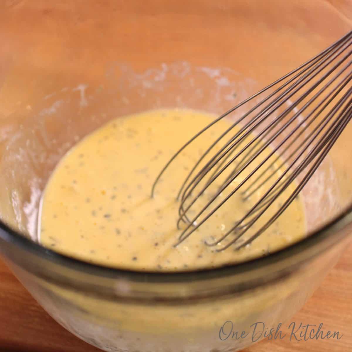 eggs and milk in a bowl next to a whisk.