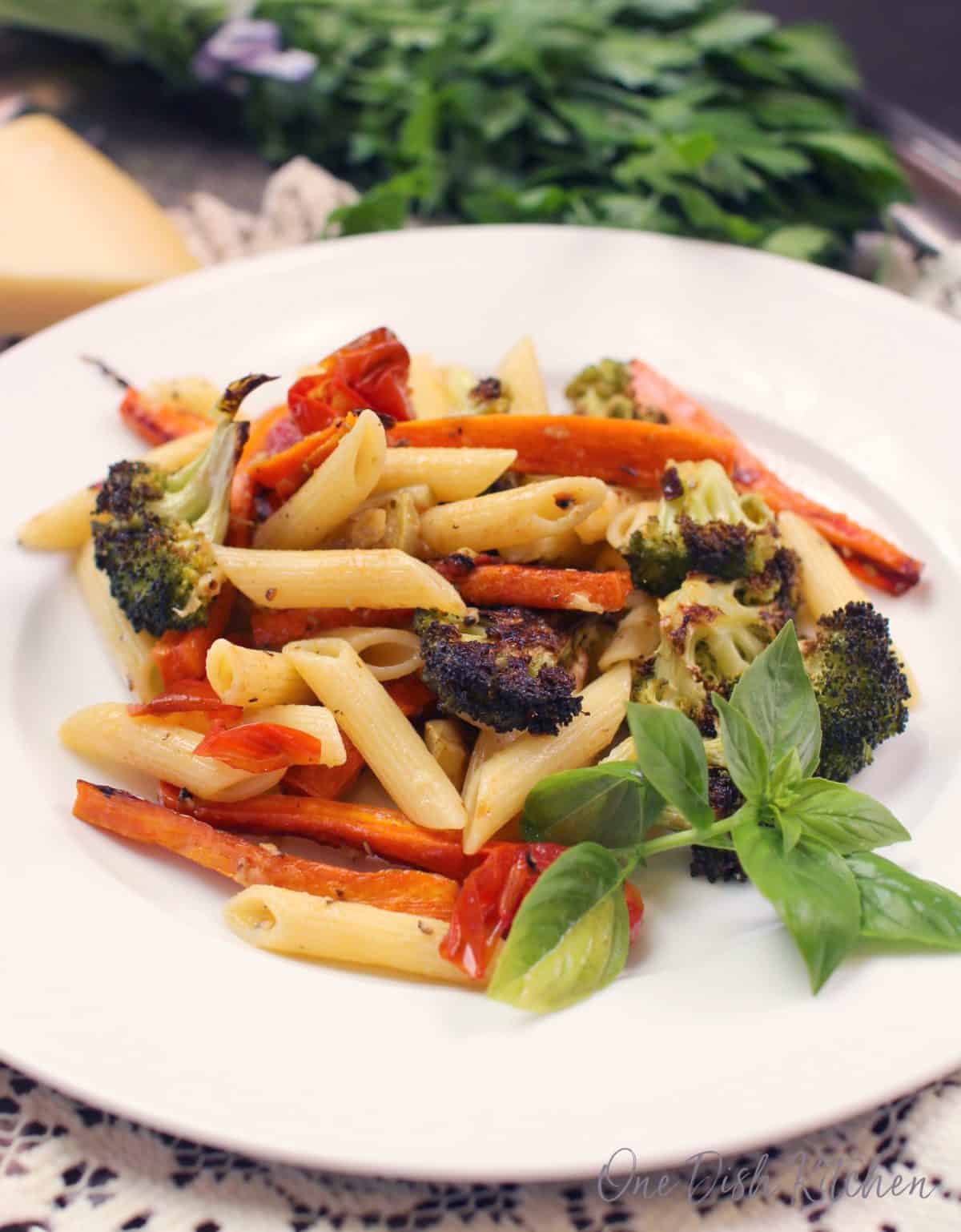 an overhead photo of a white plate filled with penne pasta, broccoli, sliced carrots, and tomatoes.