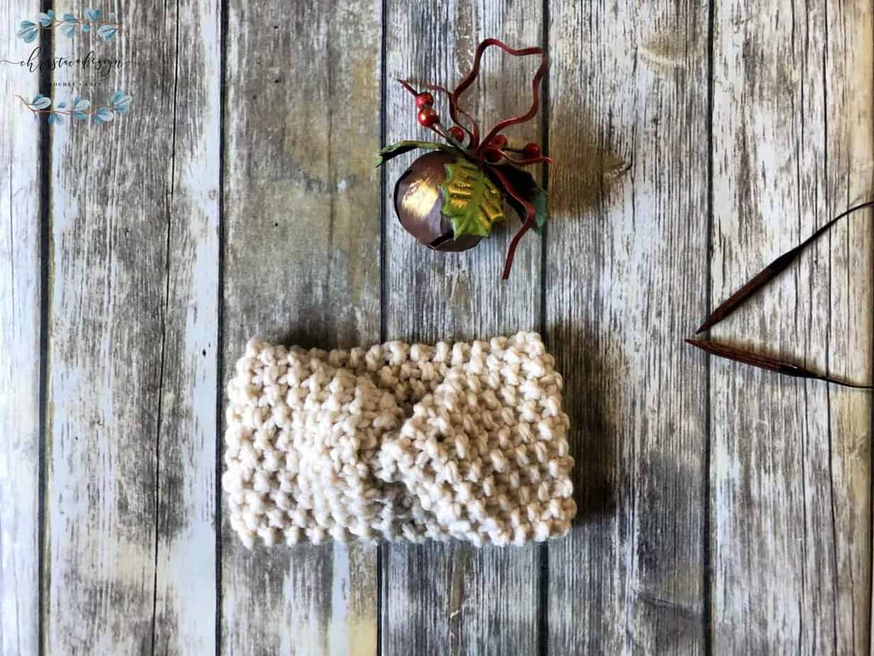 picture of chunky knit ear warmer in cream flat with Christmas bell and needles