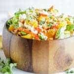 A wooden bowl packed with an Asian Cabbage Salad and a jar of asian cabbage salad dressing.