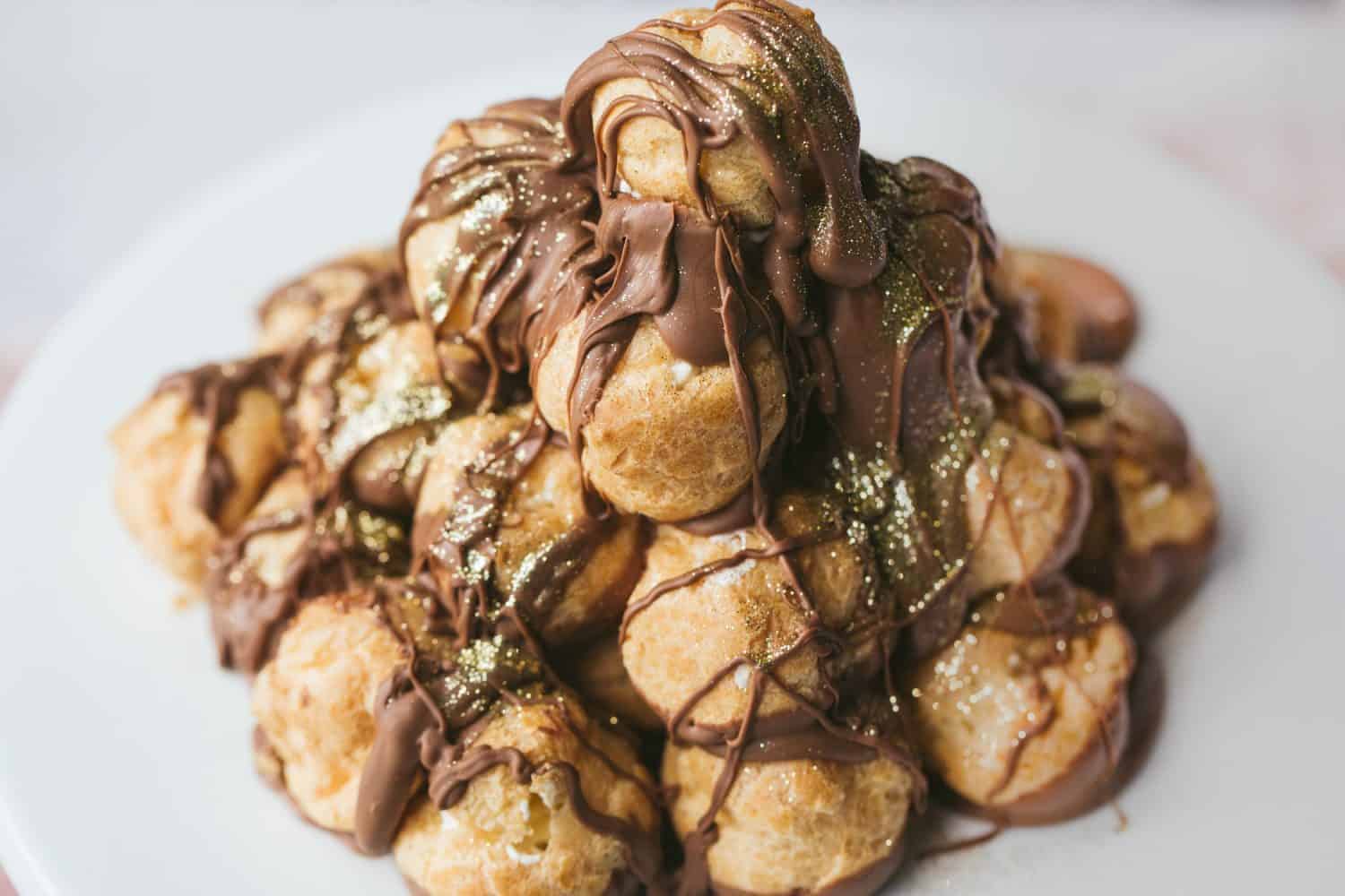Profiteroles que foram empilhados numa torre em forma de cone e depois cobertos com molho de chocolate.