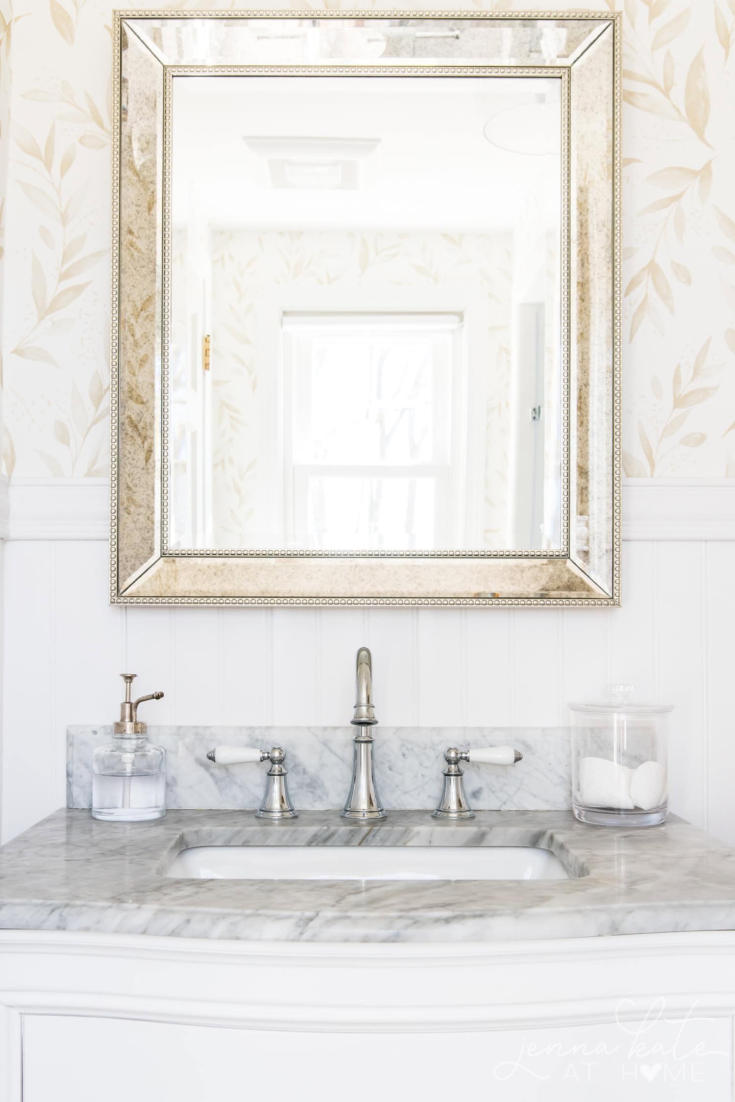 Reflection of bathroom in the mirror over the marble topped vanity with chrome faucets.