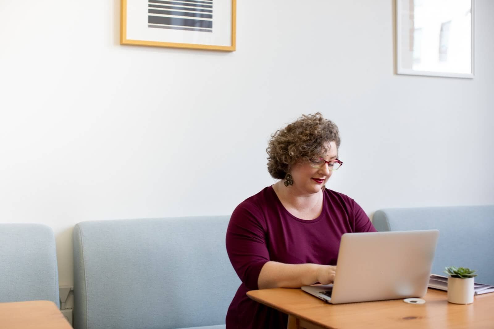 Woman with curly hair and glasses working on laptop