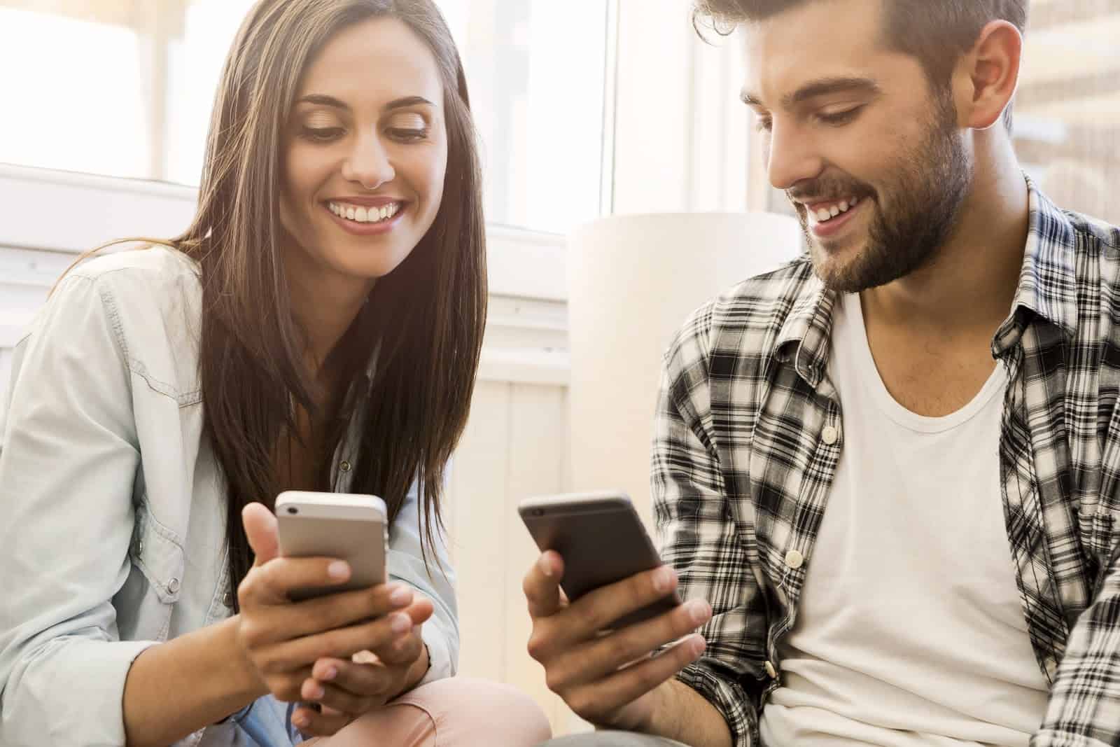 Man and woman smile while holding their phones