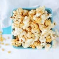 an overhead shot of stovetop kettle corn in a turquoise ceramic basket, with white background
