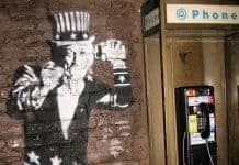 Uncle sam, rendered in graffiti on brick wall, next to a payphone wiretapping your calls