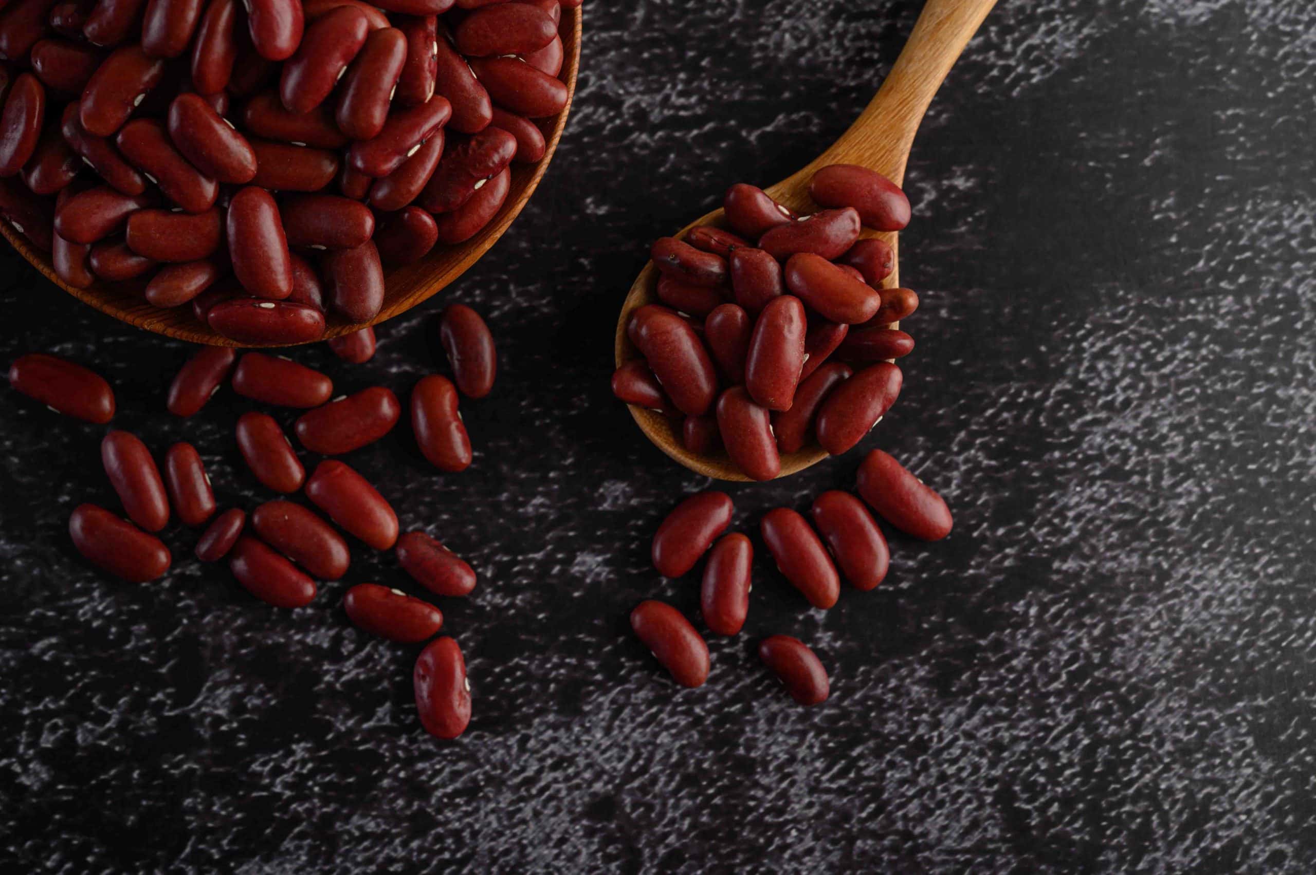 Red beans in a wooden bowl and wooden spoon on the black cement floor