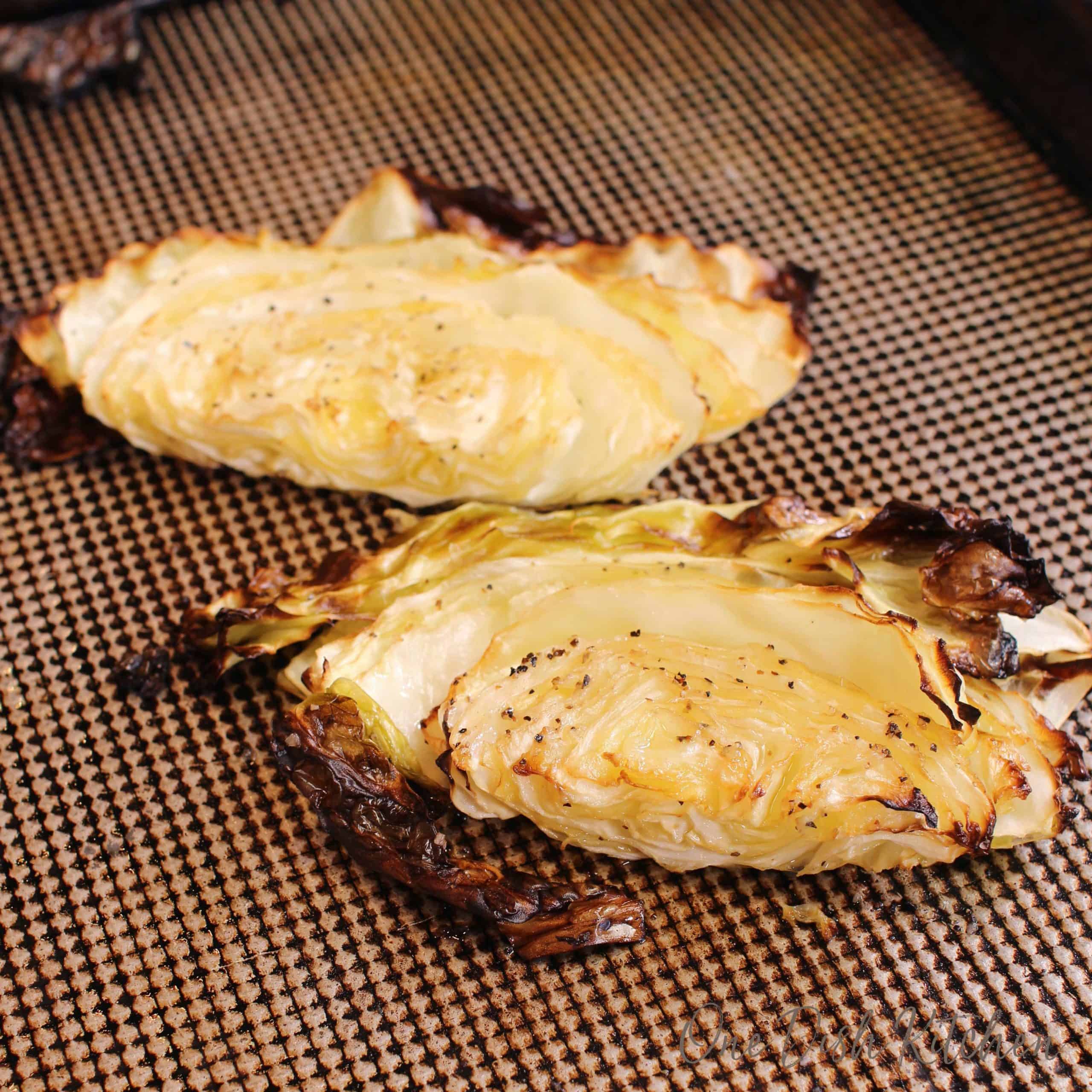 two roasted cabbage wedges on a silver baking sheet