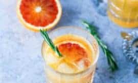 glass of blood orange mocktail on a marble surface with sliced oranges