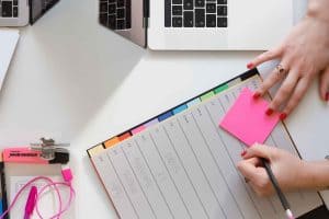 Photo of someone writing on a sticky note with a planner. Photo by Marten Bjork.