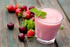 Strawberry fruit drink juicing at home with glass of strawberry fruit drink surrounded by fruits on wooden table