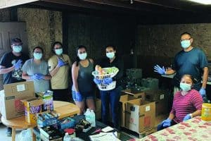 Seven people, all wearing masks and rubber gloves, pose beside boxes of supplies.