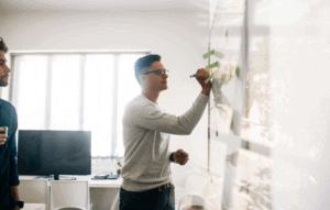 mid 30s man with glasses writing on white board to representManaging the Highs & Lows of Being an Entrepreneur