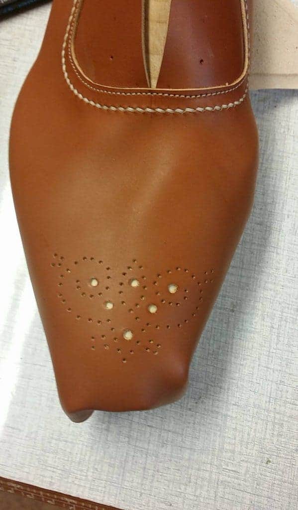 Below the medallion a light coloured leather piece is placed, which shines through the holes, matching well with the decoration stitch.