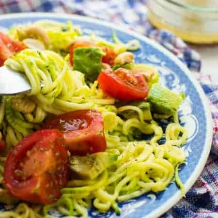 Vegan avocado zucchini salad served a blue plate with dressing on the side