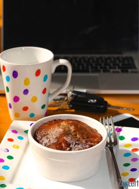 Banana bread in a small ramekin on a plate with rainbow polka dots next to a matching coffee much and a laptop computer
