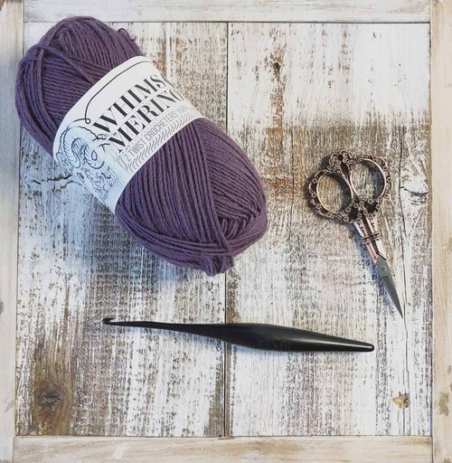 picture of one ball Whims Merino yarn in purple with wood crochet hook and scissors