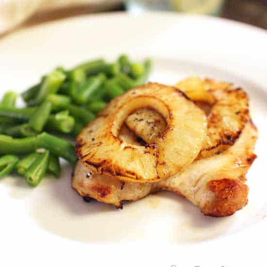 broiled chicken on a white plate next to green beans.