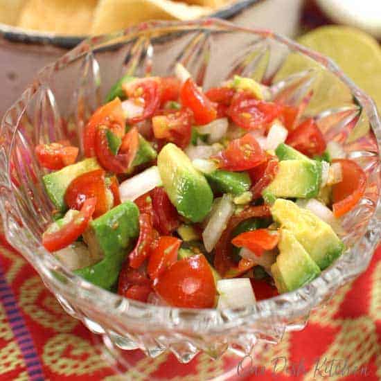 un bol de pico de gallo avec des avocats hachés sur le dessus entouré d'une nappe rouge et jaune.